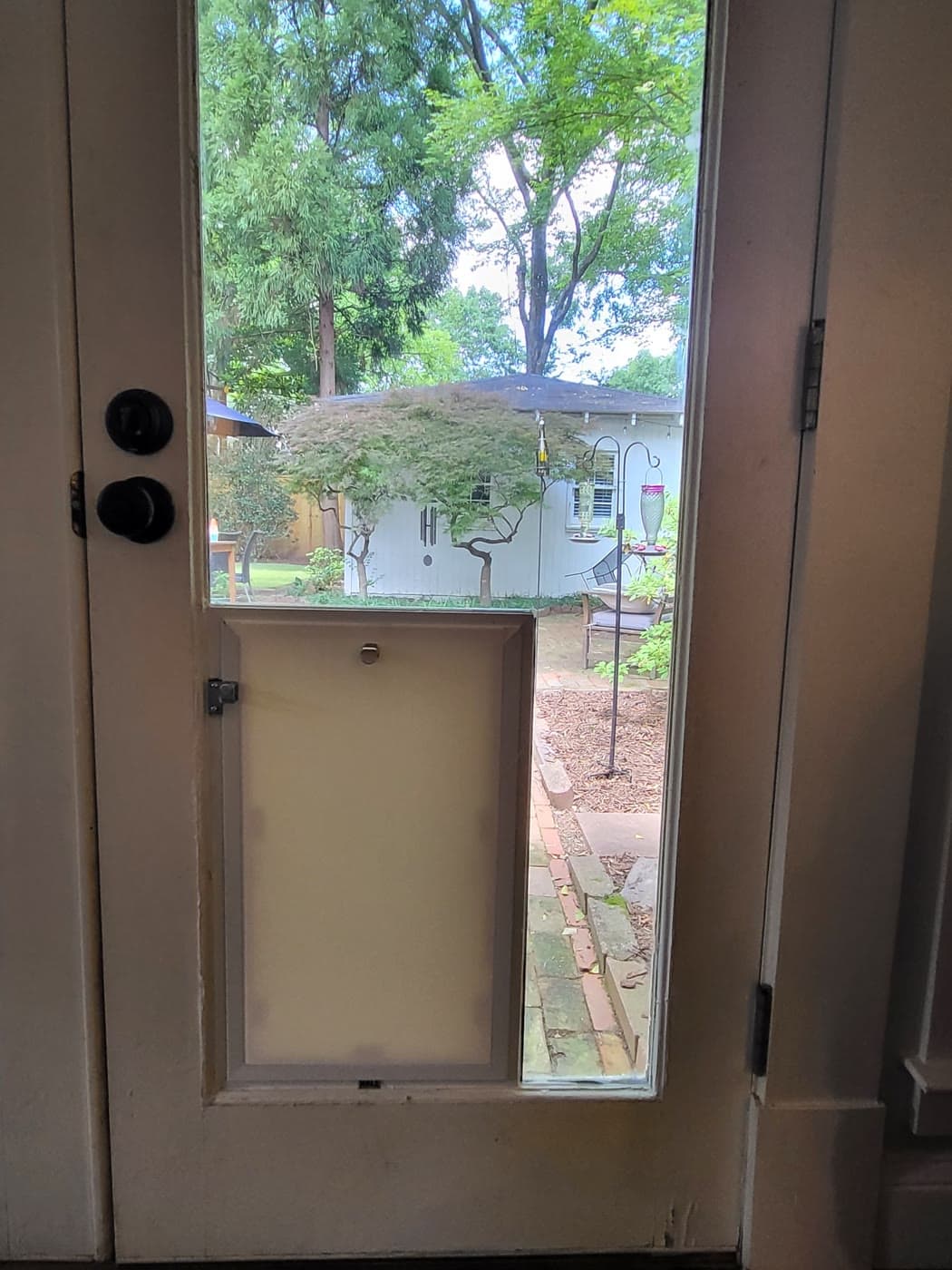 A white pet door fitted into a glass-paned door overlooking a backyard garden
