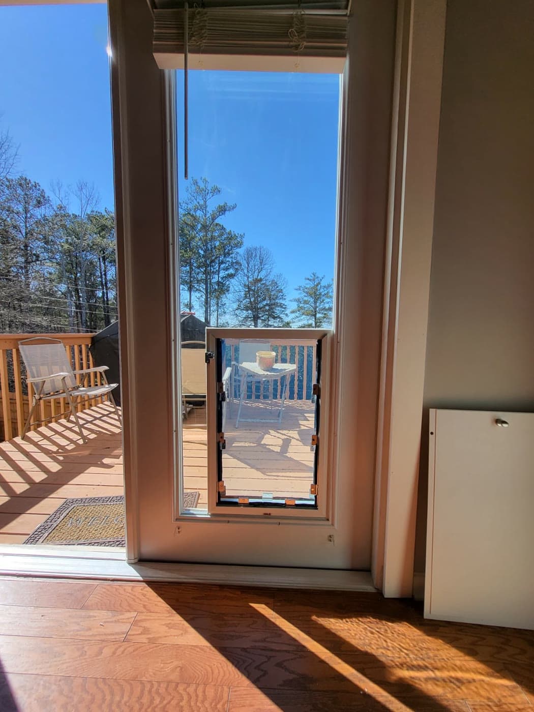 A pet door installed in a glass sidelight beside a patio door, flap open to the deck
