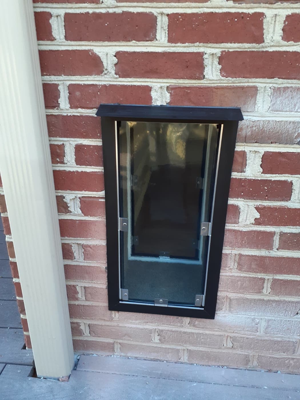 A black-framed pet door fitted neatly into a red brick wall