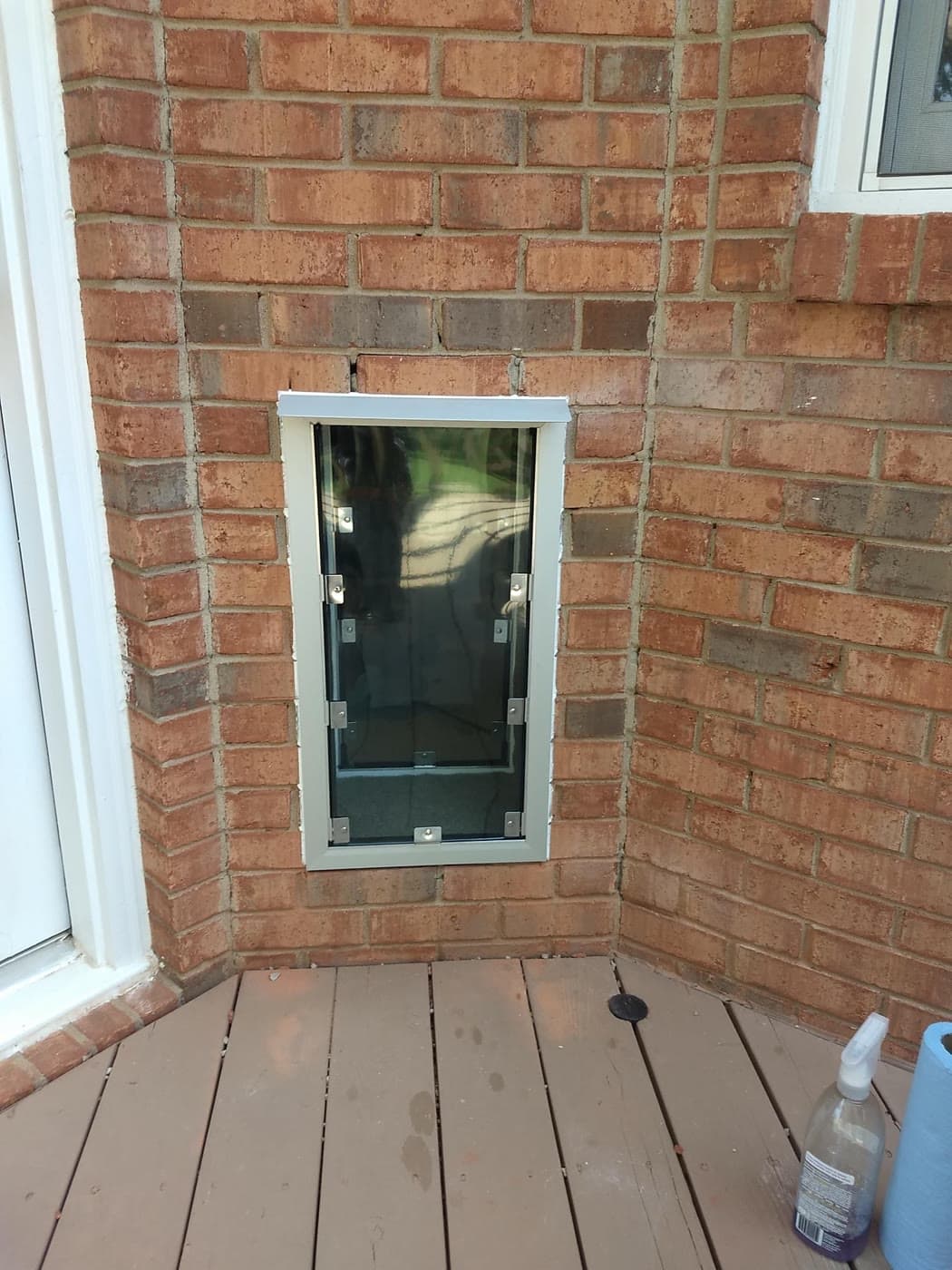 A pet door installed through a red brick wall opening onto a back deck