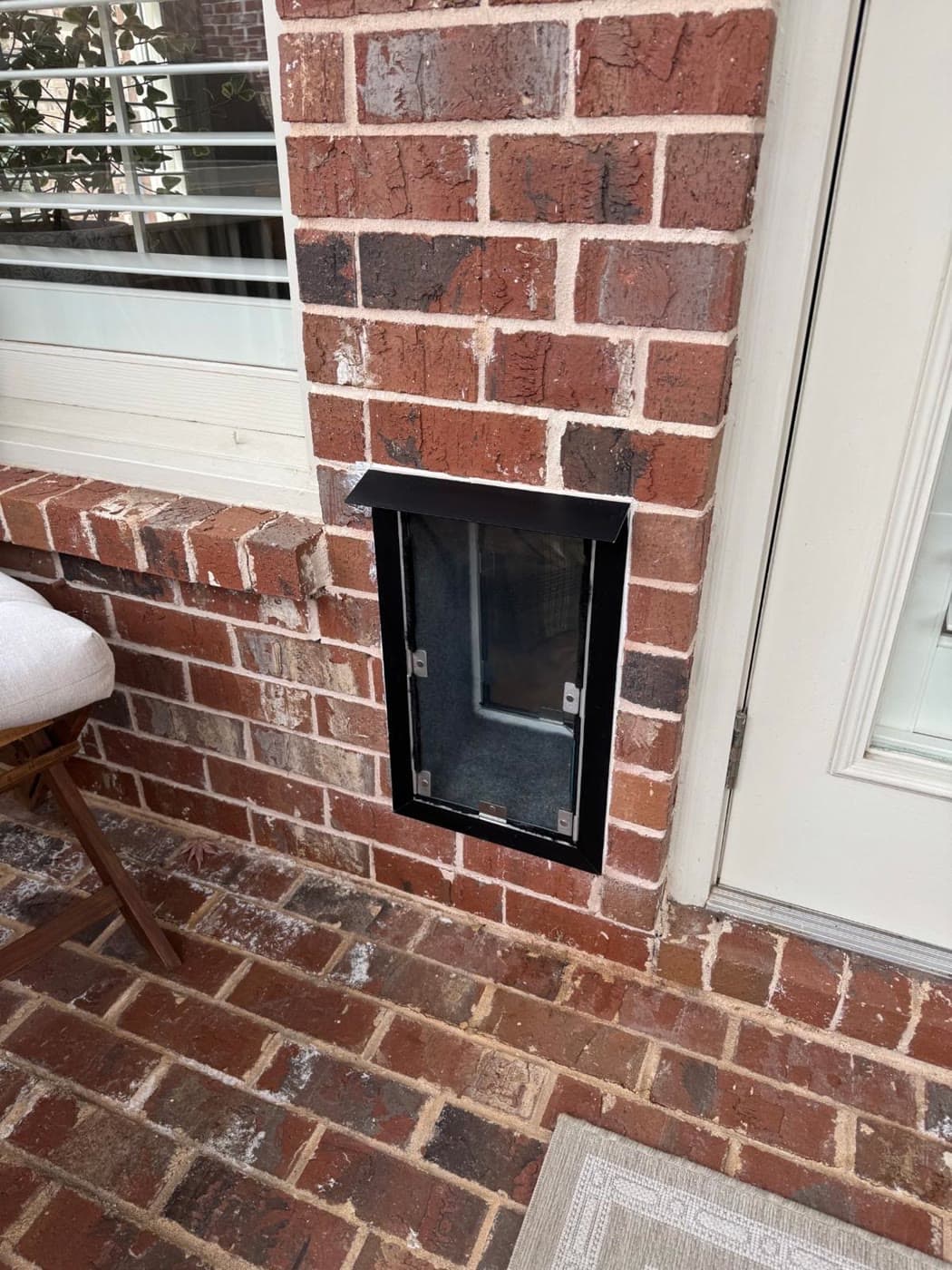 A black-framed pet door professionally installed through a red brick wall beside a patio door